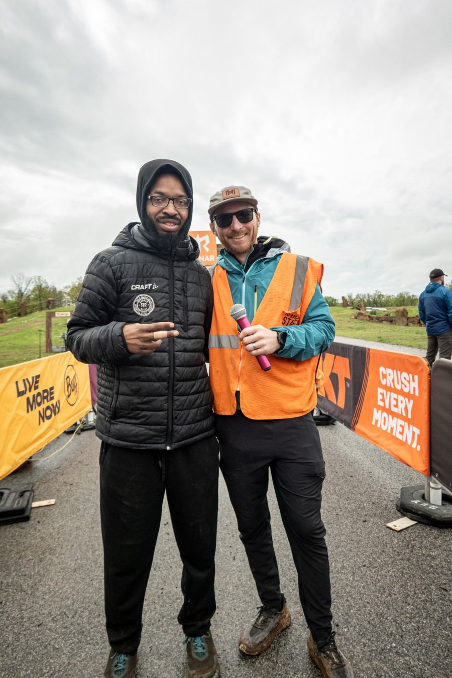 Nick Edwards in a staff vest holding a microphone beside a runner at the Ragnar Relay finish